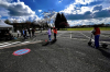 Le moniteur Antoine Chapeau conseille des élèves en trottinettes électriques dans un collège sur le parking sous un ciel bleu et nuages blancs, auto ecole holidays